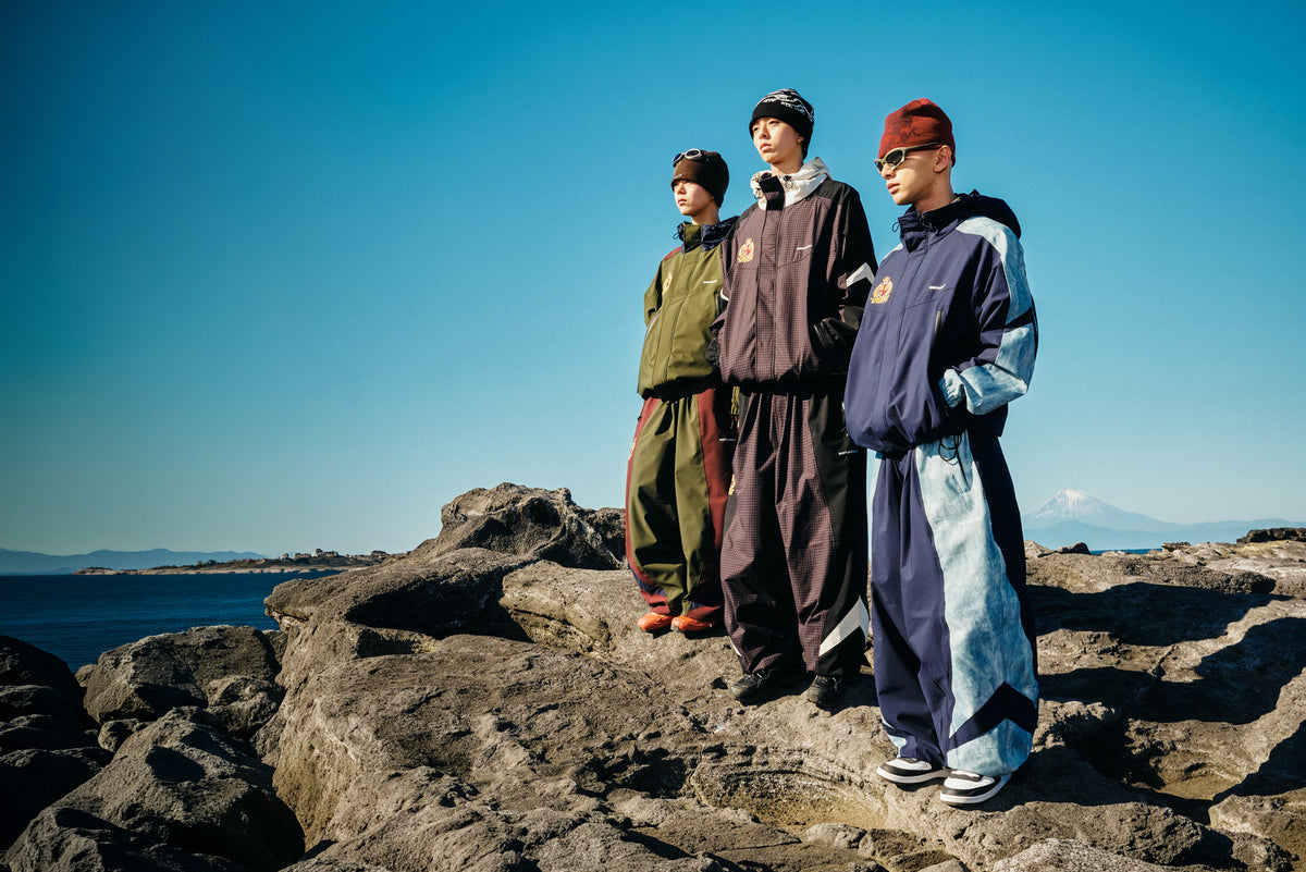 Three models wearing BSRABBIT 26/27 FW technical outerwear on a rocky coastline