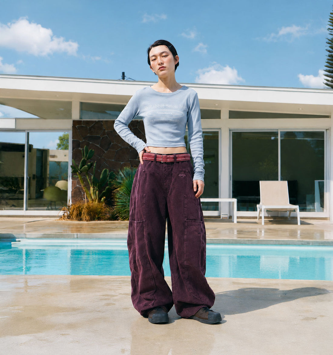Model wearing a grey cropped long sleeve top and burgundy washed wide pants by the pool